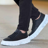 Black lace-up sneakers with chunky white sole, worn with dark pants