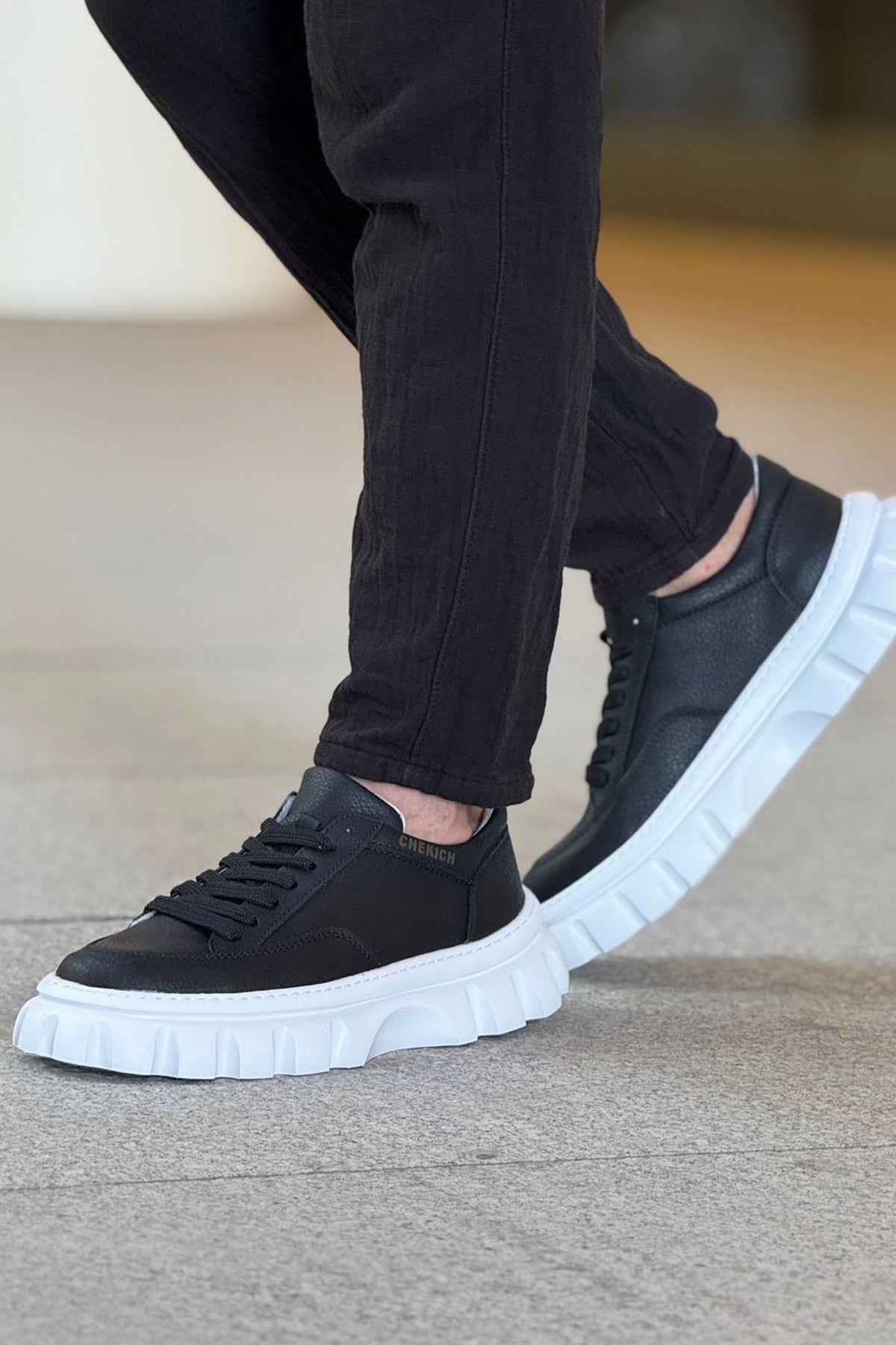 Black lace-up sneakers with chunky white sole, worn with dark pants