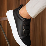 Black low-top sneaker with white sole, strap detail on the side, and padded collar.