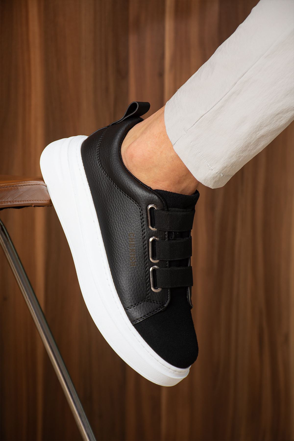 Black low-top sneaker with white sole, strap detail on the side, and padded collar.
