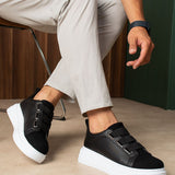 Black low-top sneakers with white rubber sole and front strap closure.