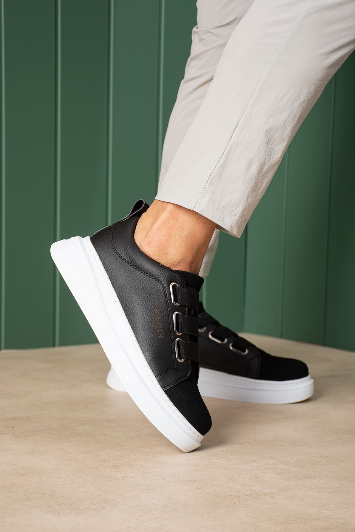 Black textured low-top sneakers with white midsole and adjustable strap across upper.