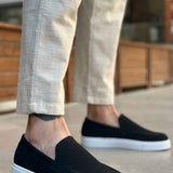 Men's black suede loafer with white rubber sole, worn with light pants