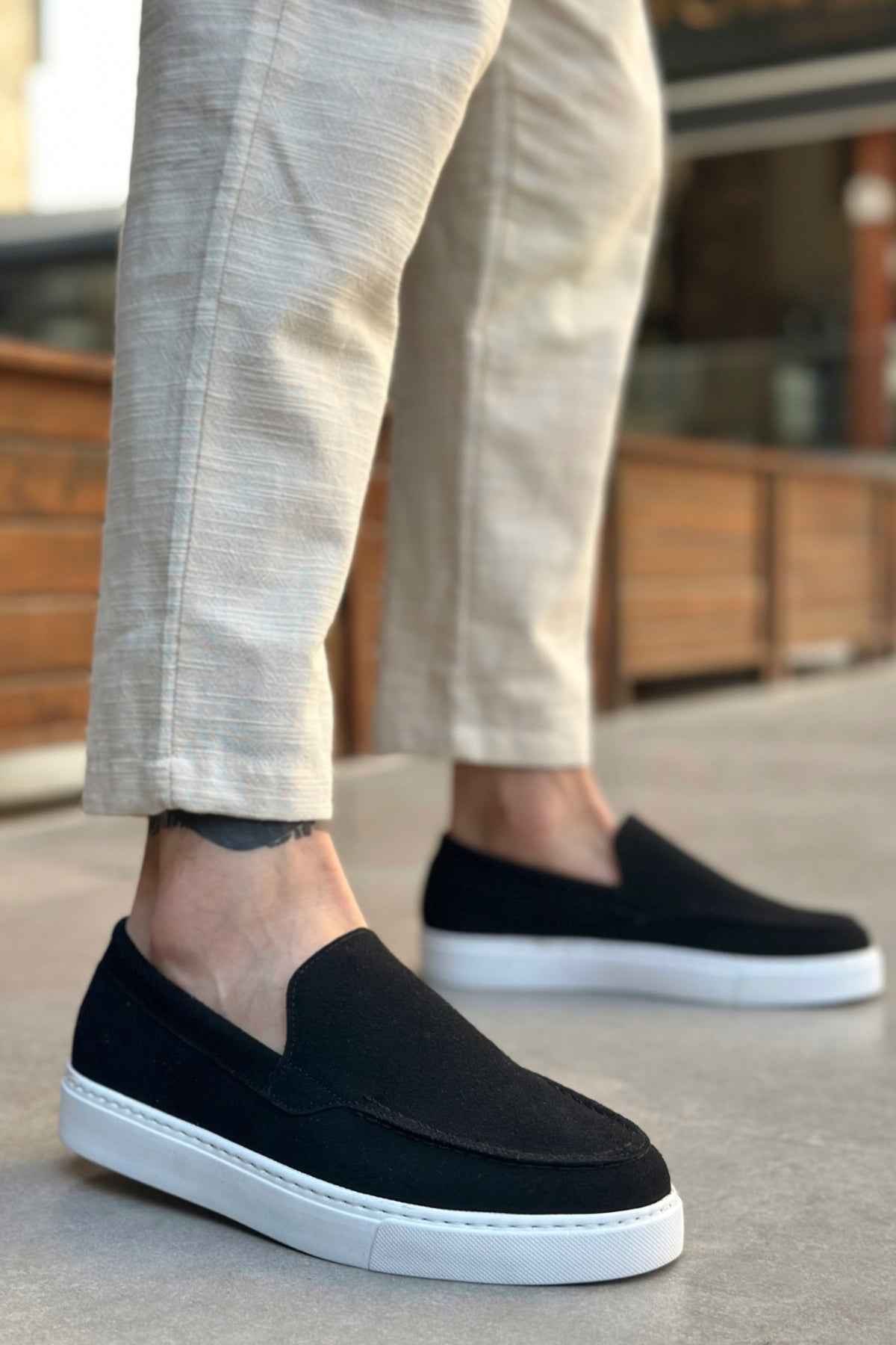 Men's black suede loafer with white rubber sole, worn with light pants