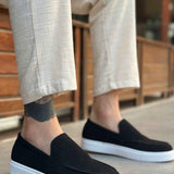Men's black suede slip-on loafer with white sole, worn with light pants
