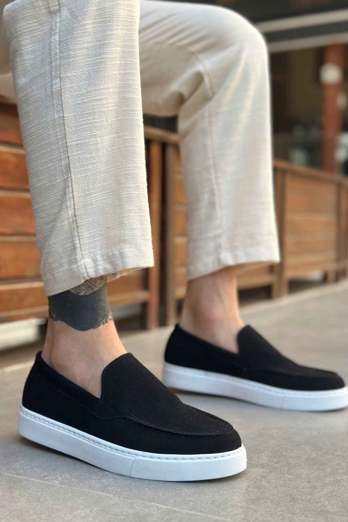 Men's black suede slip-on loafer with white sole, worn with light pants
