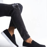 Men's black suede slip-on loafers with white sole, worn with dark jeans