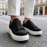Black suede sneakers on feet, lace-up design and white platform sole