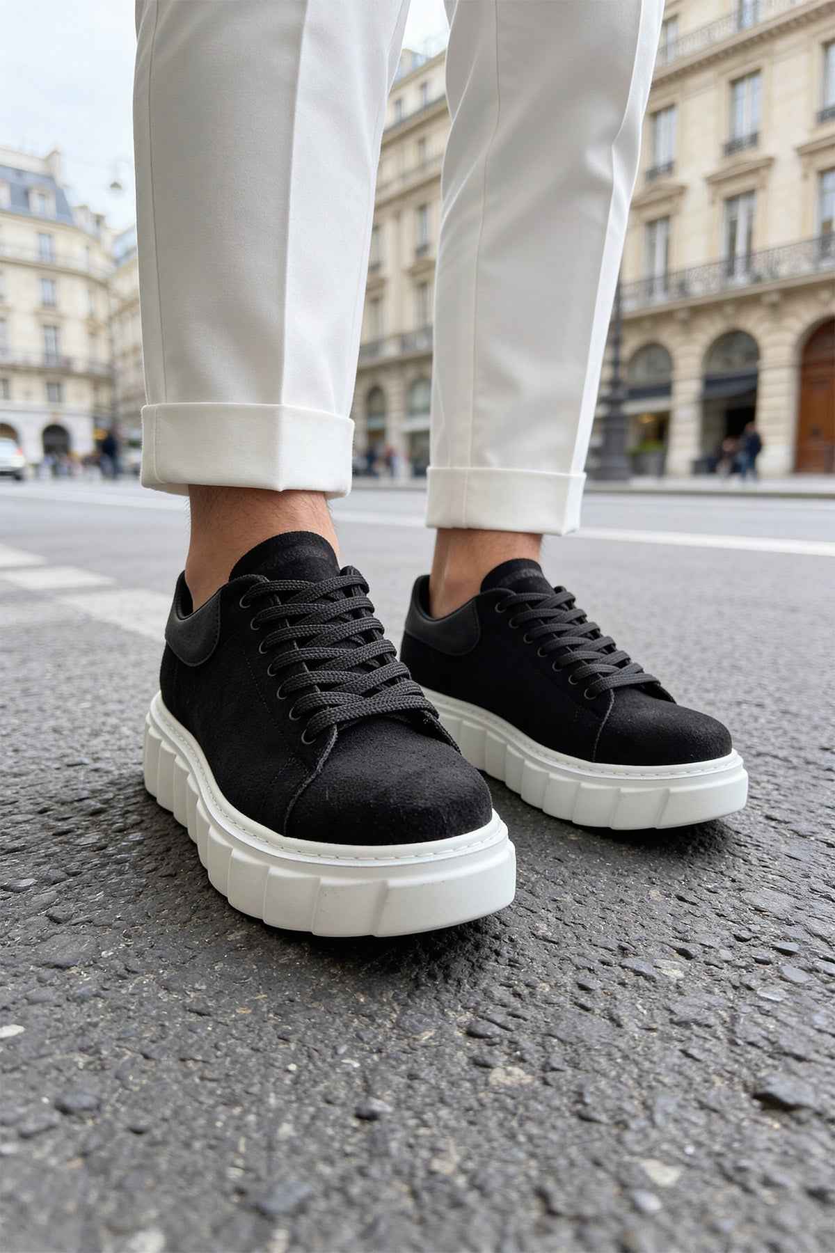 Black suede sneakers on feet, lace-up design and white platform sole