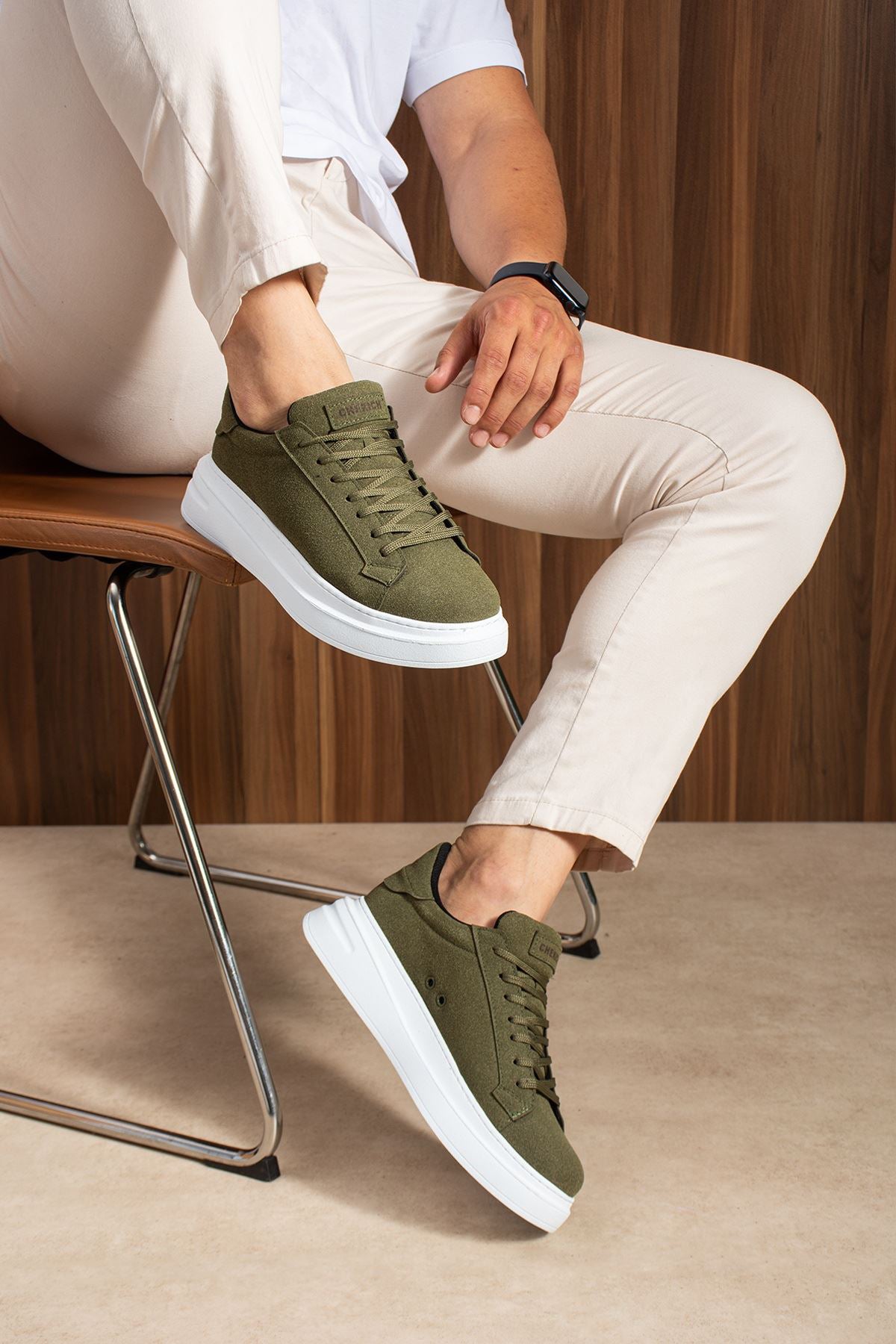 Men's olive suede low-top sneakers, lace-up, white soles, seated leg pose