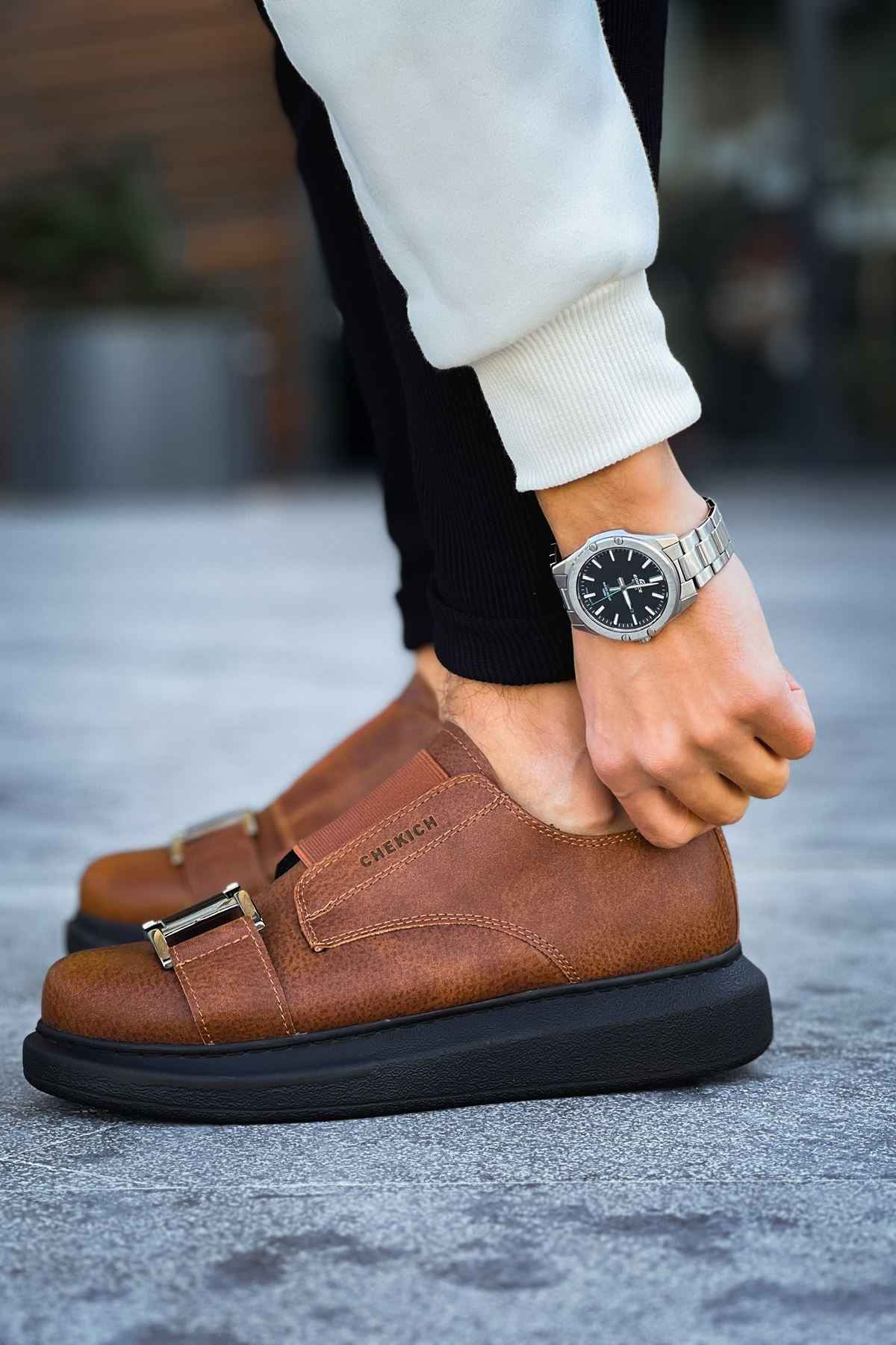 Men’s casual tan sneakers with double buckle straps, black sole, worn with dark pants