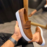 Tan suede loafer with strap and white sole, shown on foot with dark jeans