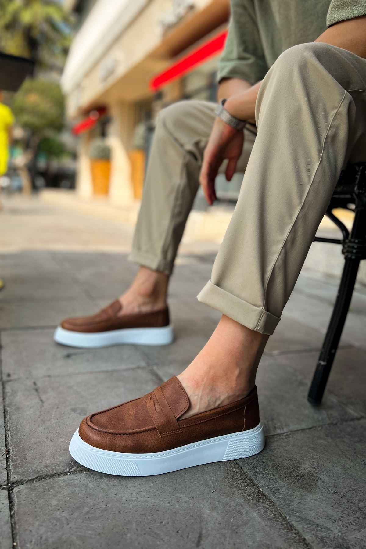Brown slip-on loafers with white rubber sole, side view.