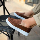 Brown slip-on loafers with white sole, vamp strap detail, close-up.