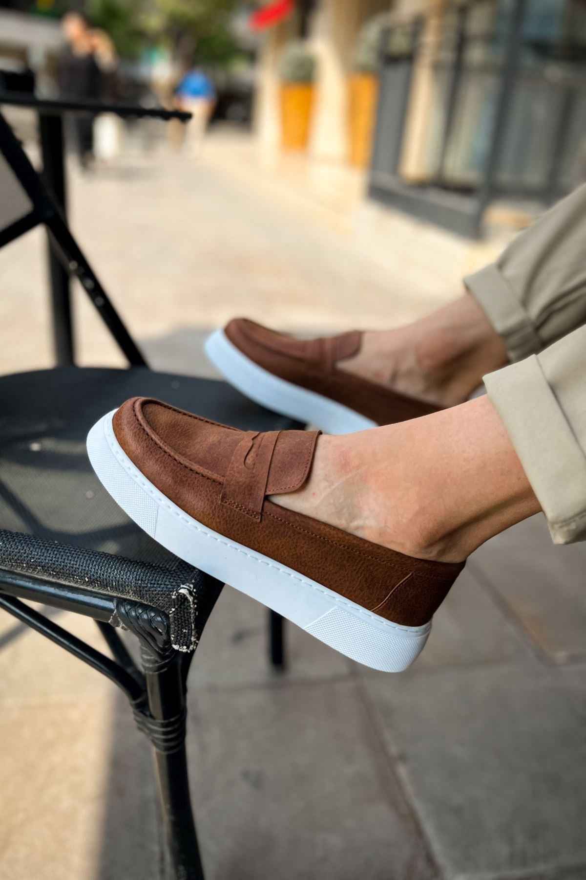 Brown slip-on loafers with white sole, vamp strap detail, close-up.