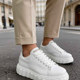 White low-top sneakers with lace-up uppers and chunky outsole, worn with pants.