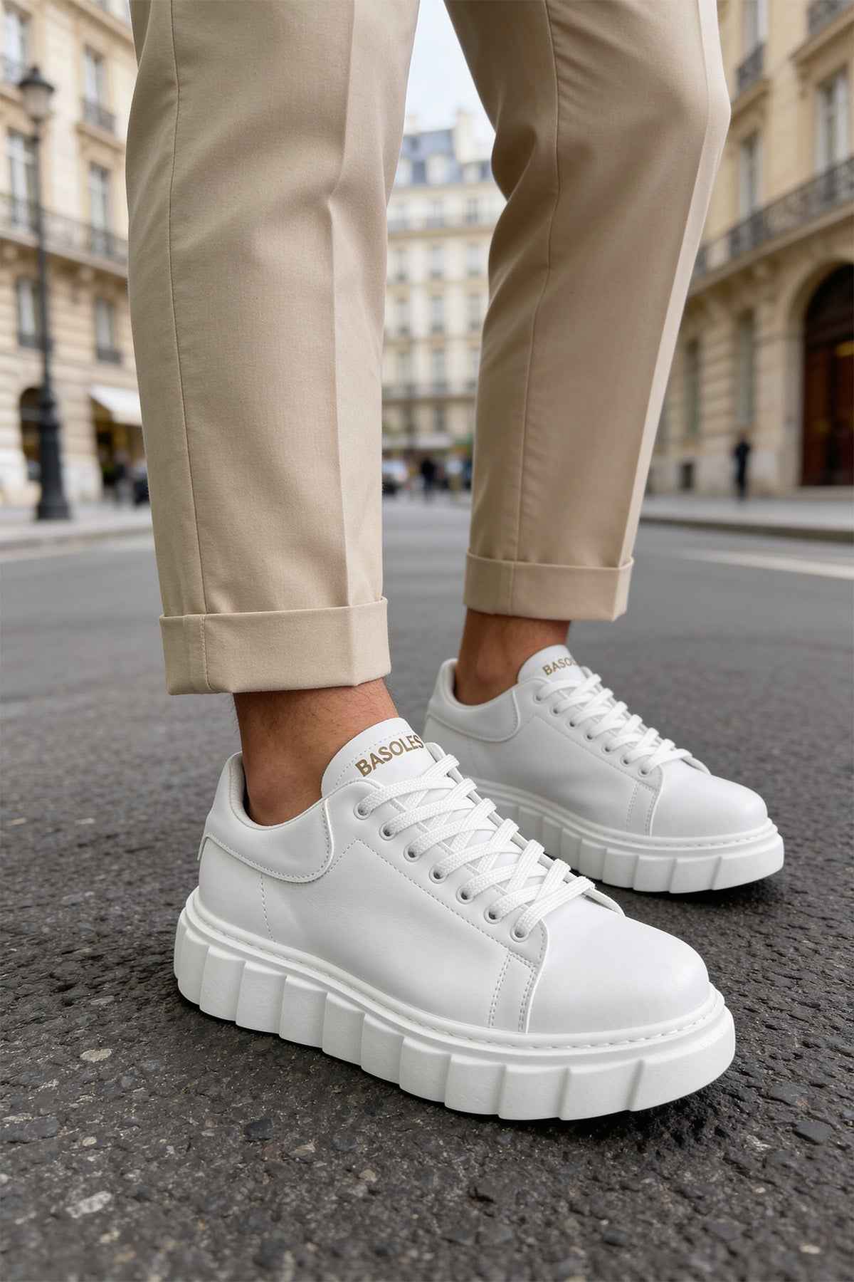 White low-top sneakers with lace-up uppers and chunky outsole, worn with pants.