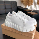 White lace-up low-top sneakers with chunky platform sole, on display box.