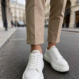 White lace-up sneakers with thick tread sole, worn with light trousers.
