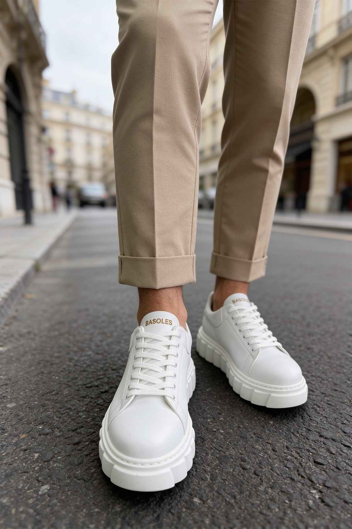 White lace-up sneakers with thick tread sole, worn with light trousers.