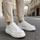 White lace-up sneakers with ridged platform sole, worn with beige ankle pants.