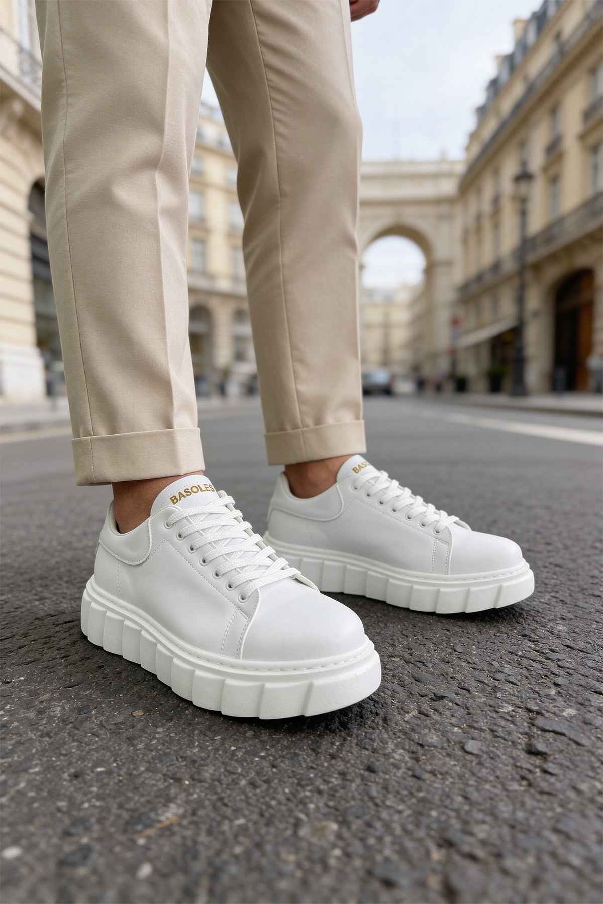 White lace-up sneakers with ridged platform sole, worn with beige ankle pants.