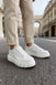 White lace-up sneakers with ridged platform sole, worn with beige ankle pants.