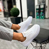 Men's white low-top sneakers on angled foot, lace-up with side texture