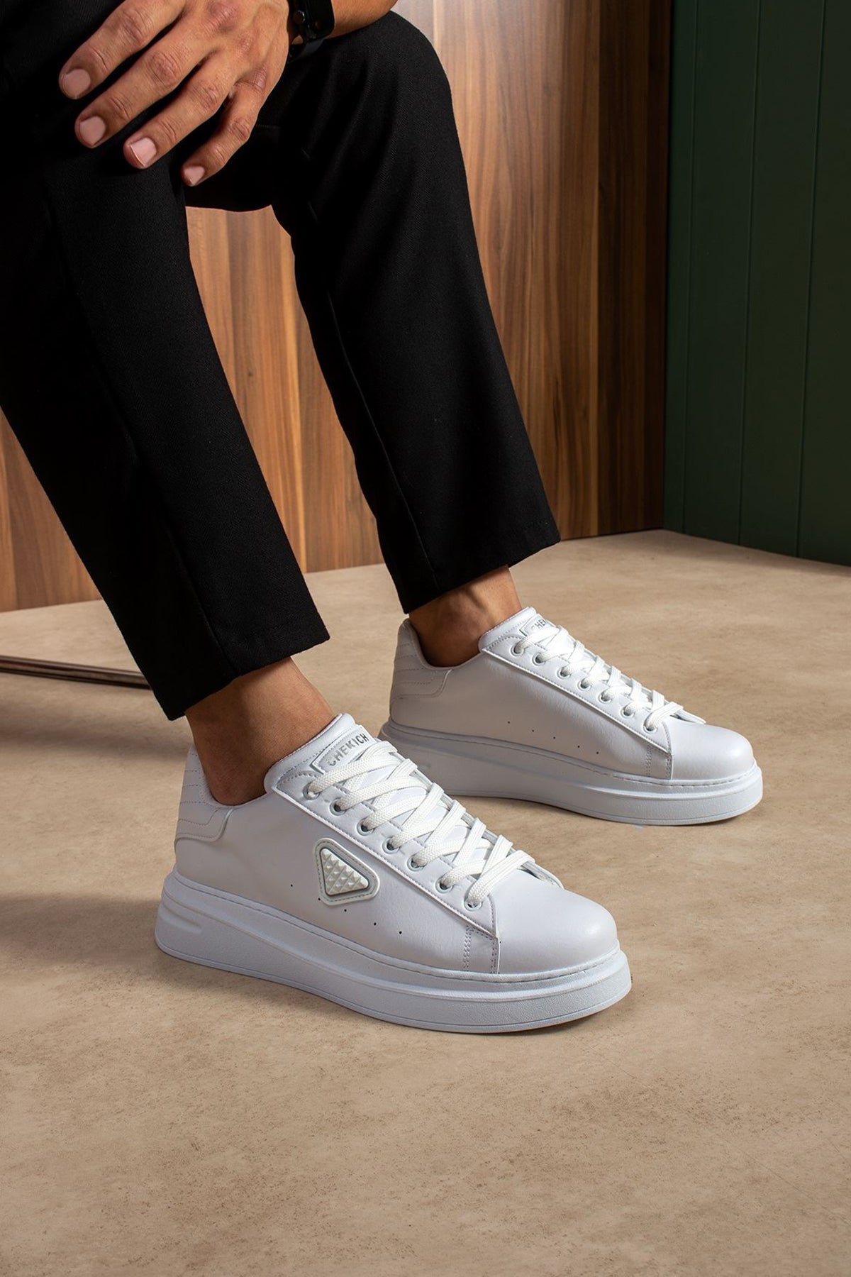 Men's white low-top lace-up sneakers with side logo patch, worn with dark pants