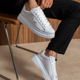 Men's white low-top lace-up sneakers, pair shown on feet beside a chair