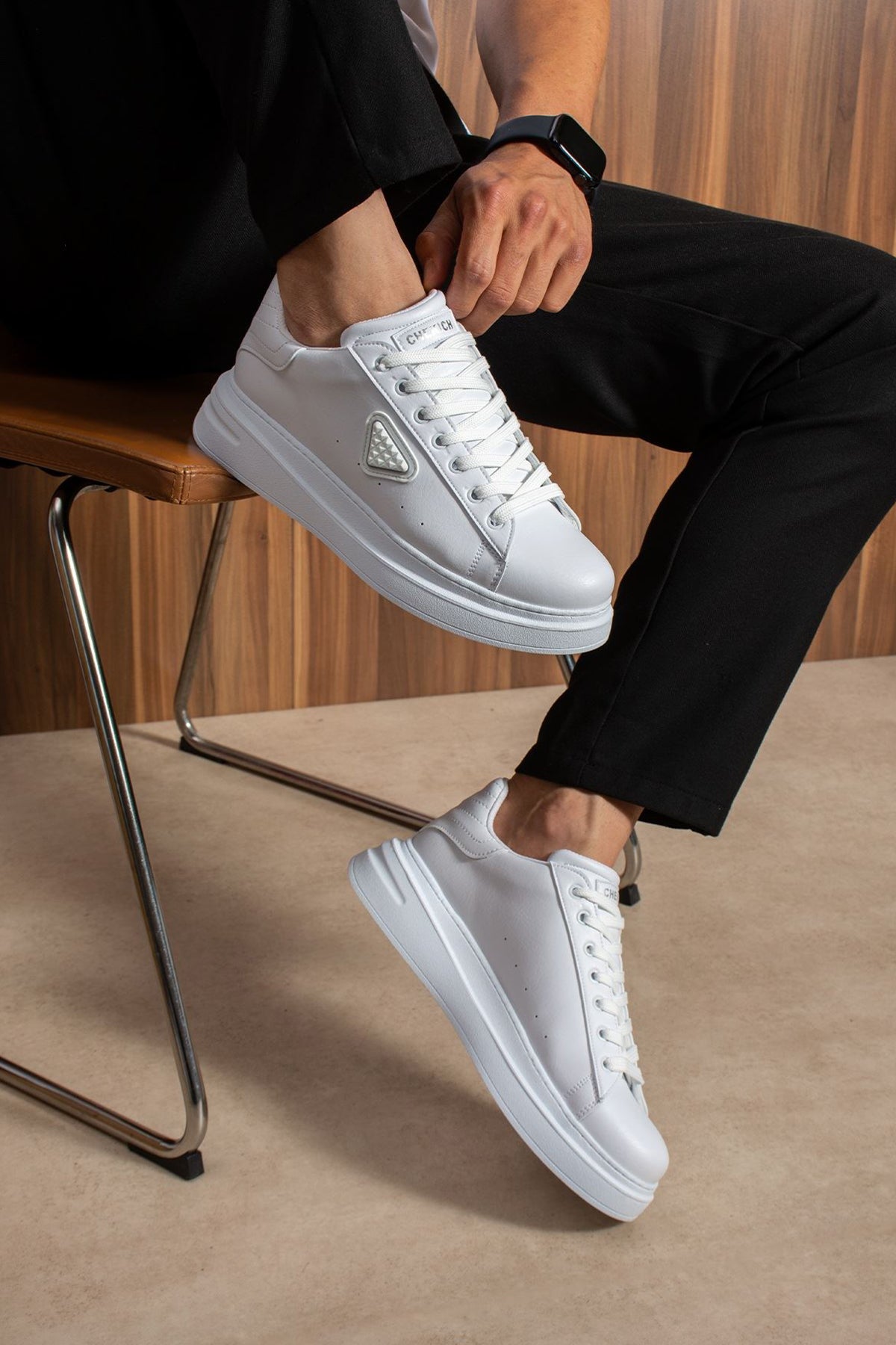 Men's white low-top lace-up sneakers, pair shown on feet beside a chair