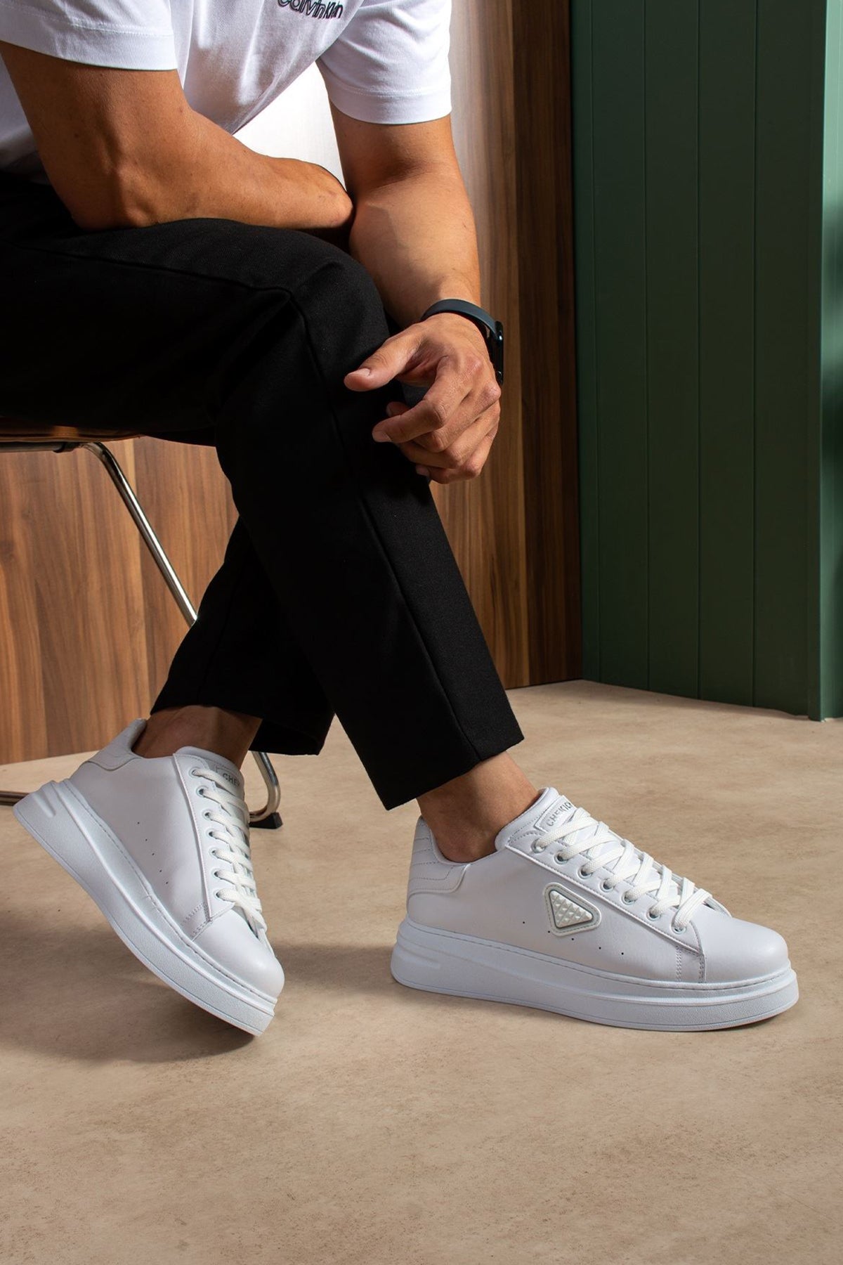 Men's white low-top lace-up sneakers with side patch, worn with black pants