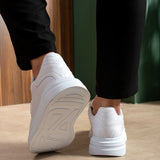 Men's white sneakers heel view with textured sole, lace-up top, worn with dark pants