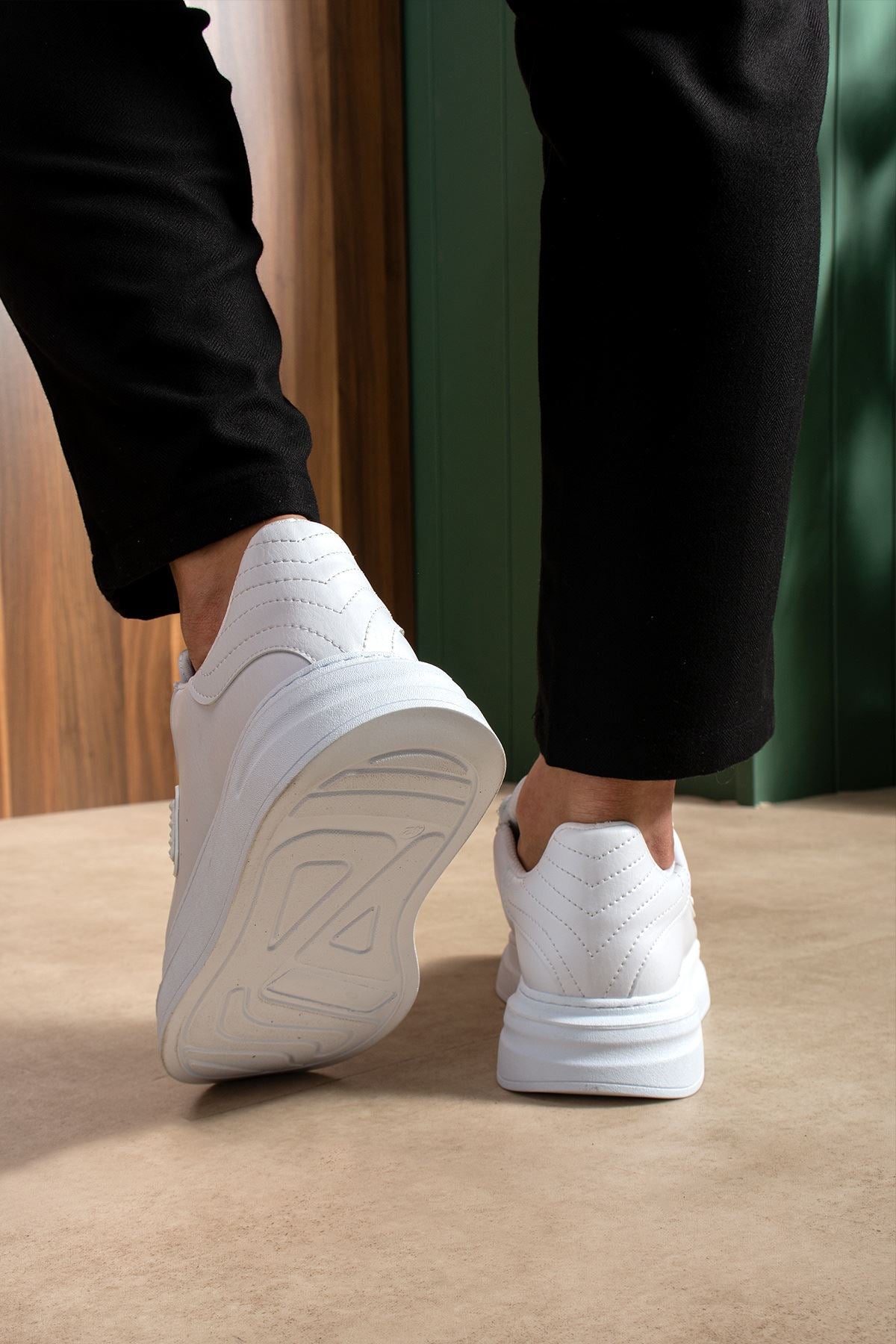 Men's white sneakers heel view with textured sole, lace-up top, worn with dark pants