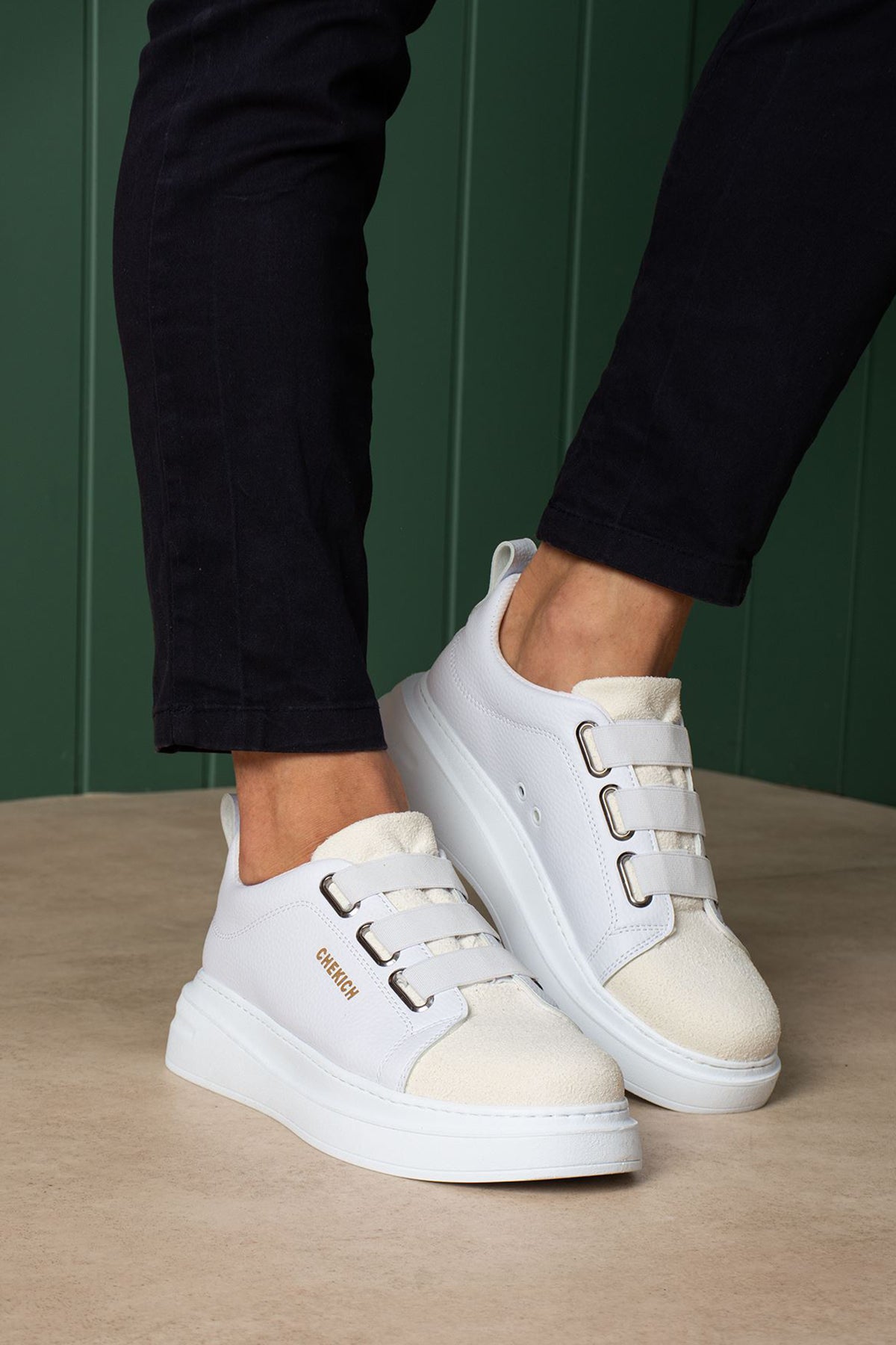 White low-top sneakers with side buckles and stitched toe cap, worn with dark pants.