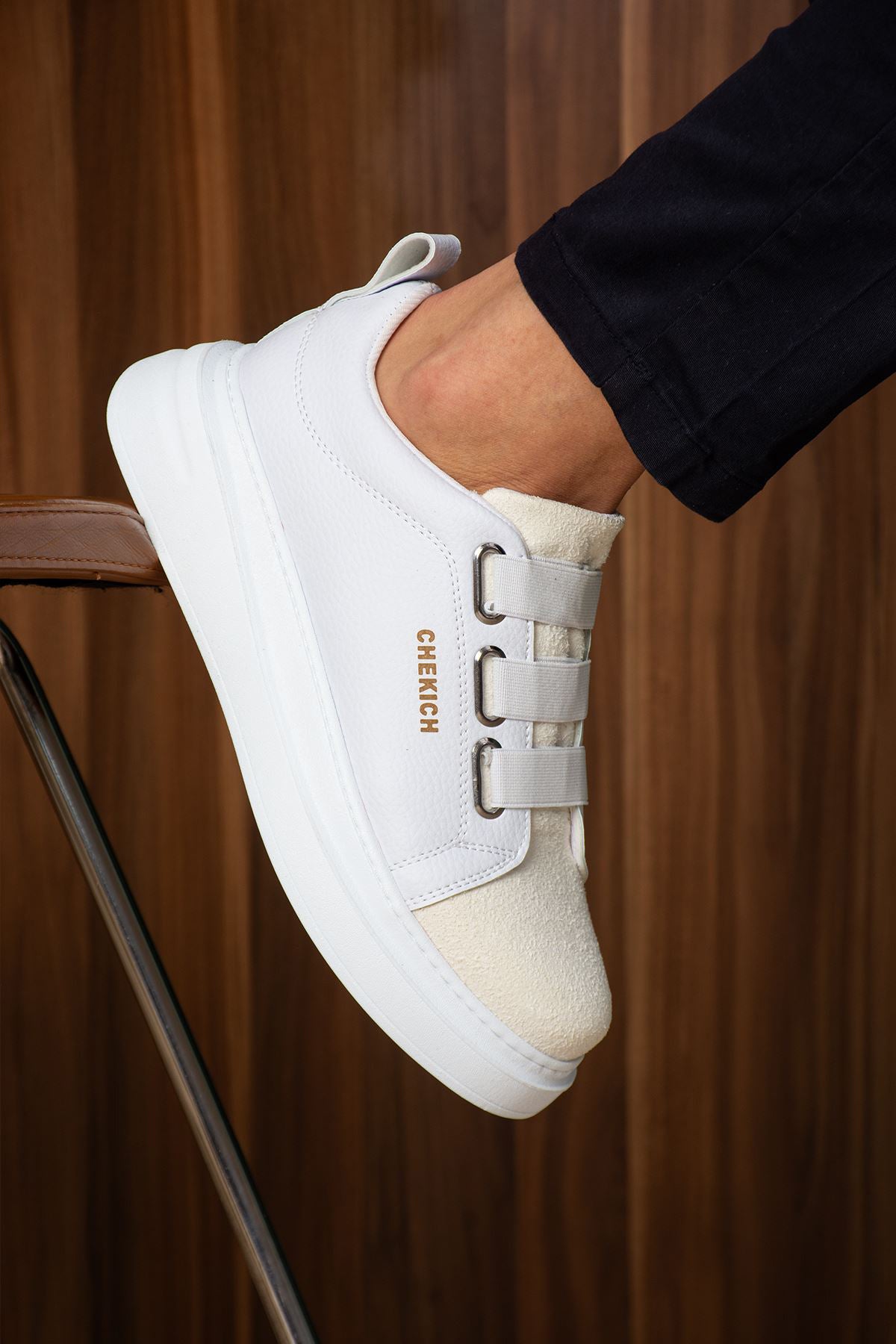 White low-top sneaker showing padded collar, side buckle straps, and logo text.