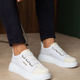 Pair of white low-top sneakers with side buckles, worn by a person standing.