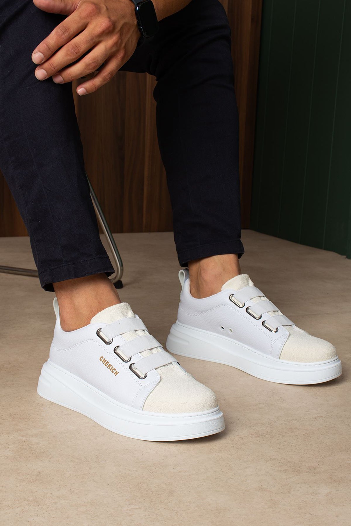 Pair of white low-top sneakers with side buckles, worn by a person standing.