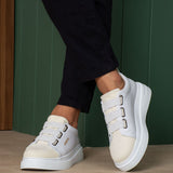 White low-top sneakers with thick sole and side buckle straps, side view on feet.