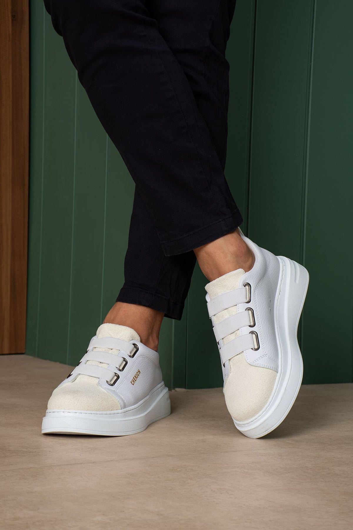 White low-top sneakers with thick sole and side buckle straps, side view on feet.