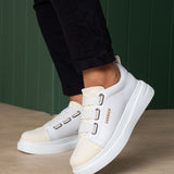White low-top sneakers with twin buckle straps and side logo lettering, angled close-up.