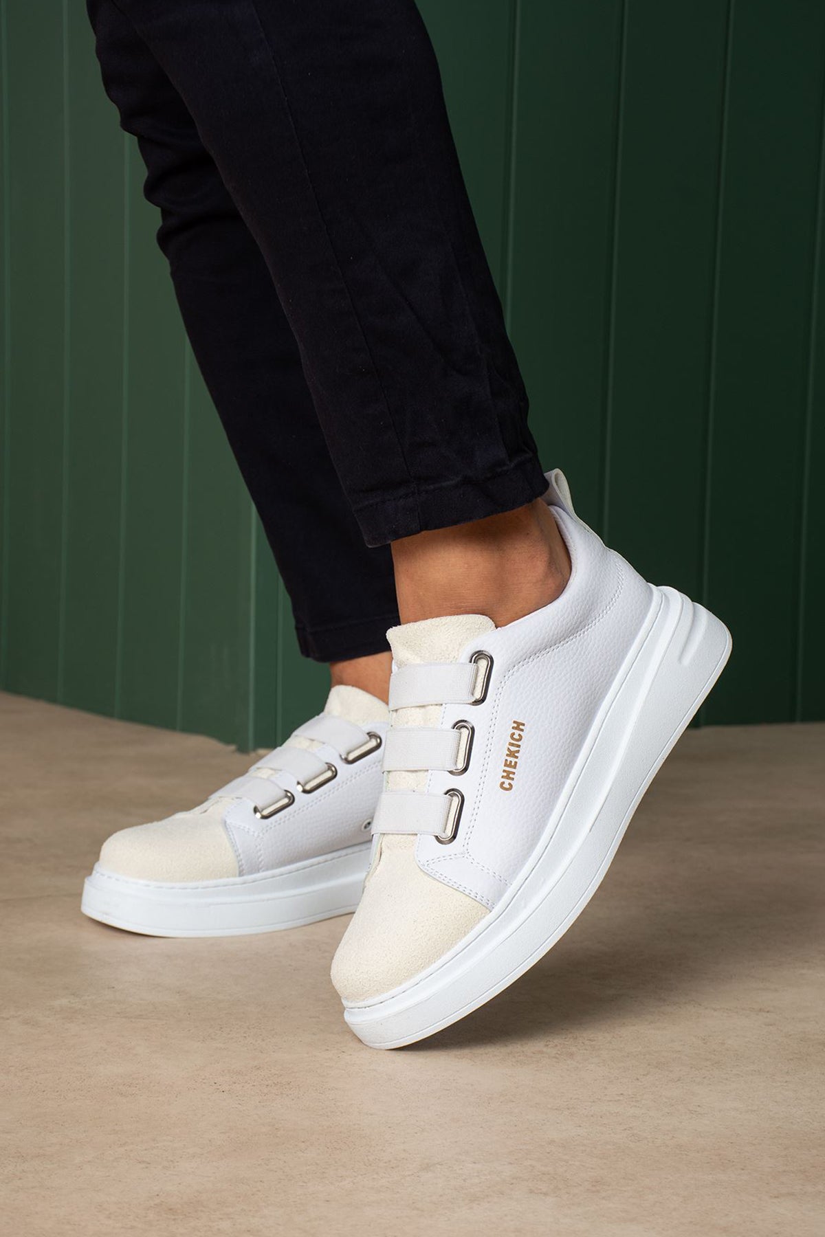 White low-top sneakers with twin buckle straps and side logo lettering, angled close-up.