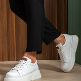 White sneakers with lace-up front, chunky sole, tan heel tab, walking stance