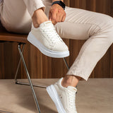 White suede sneakers on model feet, lace-up design and blue-gray platform sole.