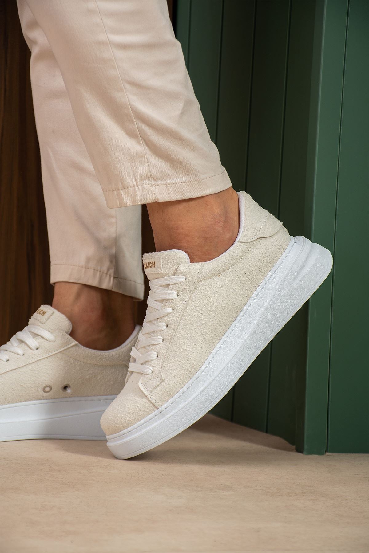 White suede sneakers in profile, lace-up tongue and thick white sole.