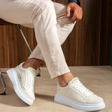 White suede lace-up sneakers on seated legs, with blue-gray rubber outsole.