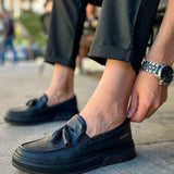 Men's black loafer with tassel detail, side view with textured sole edge.