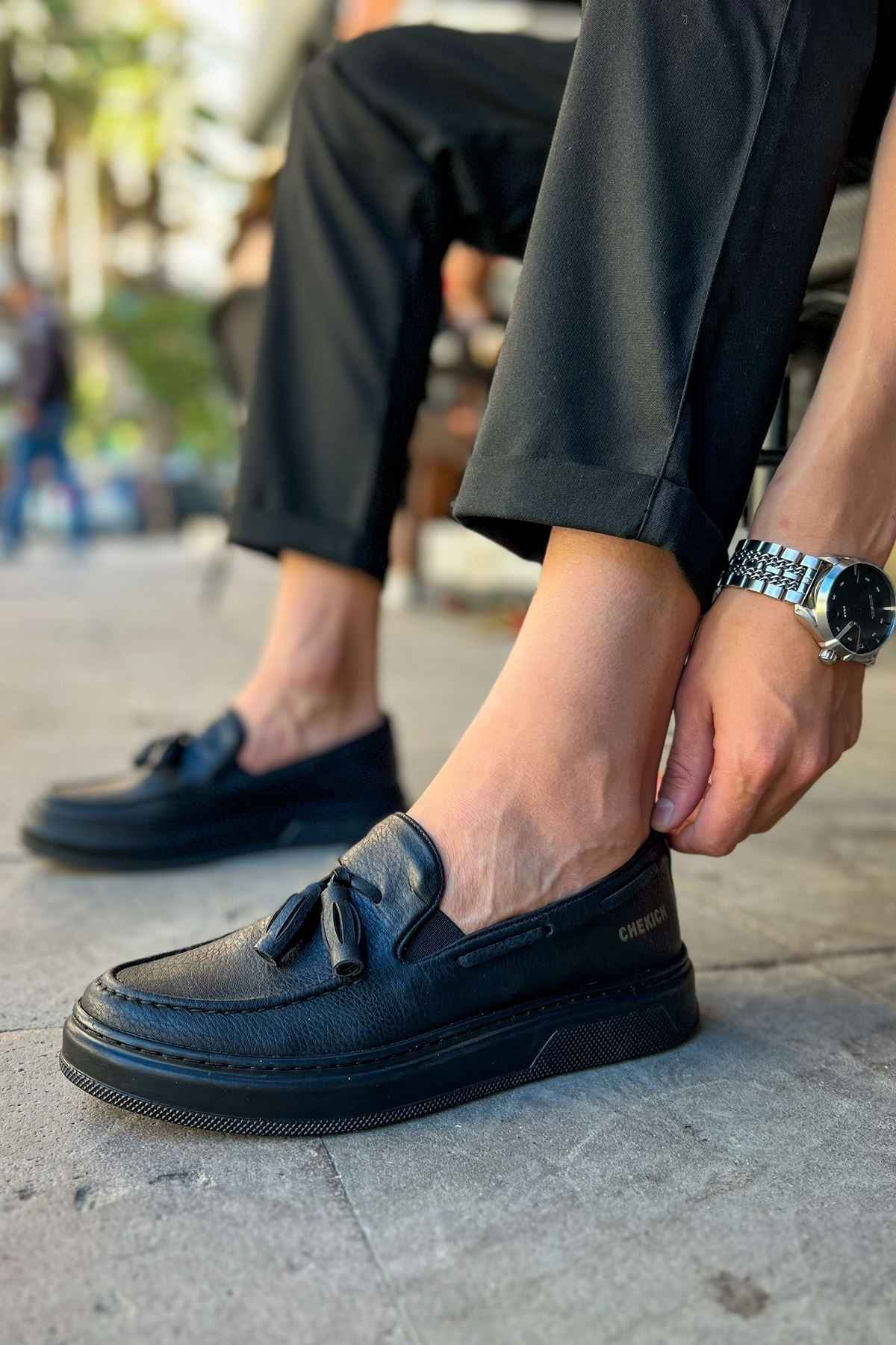 Men's black loafer with tassel detail, side view with textured sole edge.