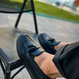 Men's black loafer with tassel detail, front angled view with stitched toe.