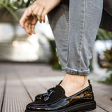 Black patent leather loafer with tassel detail, worn with light blue jeans